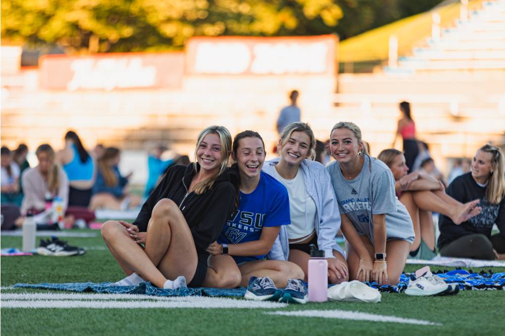 Four students smiling on the Football Field during a yoga session at sunset